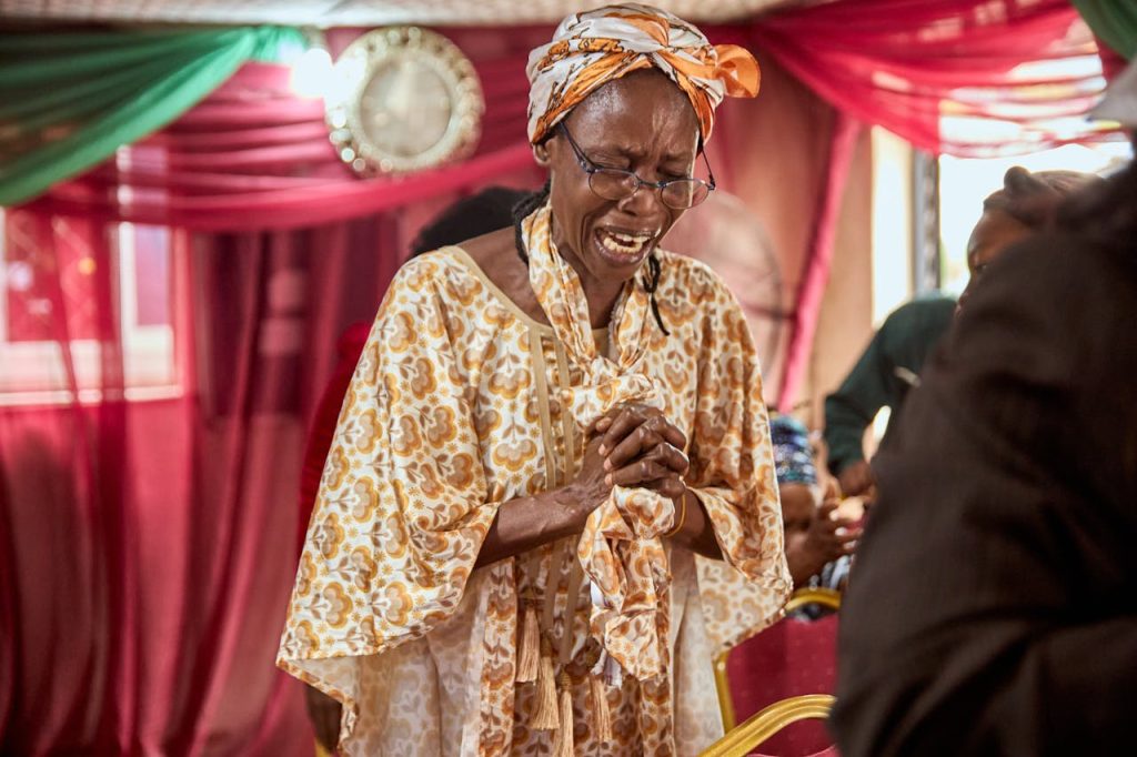Elderly woman engaged in prayer at a colorful church service, conveying deep emotion.